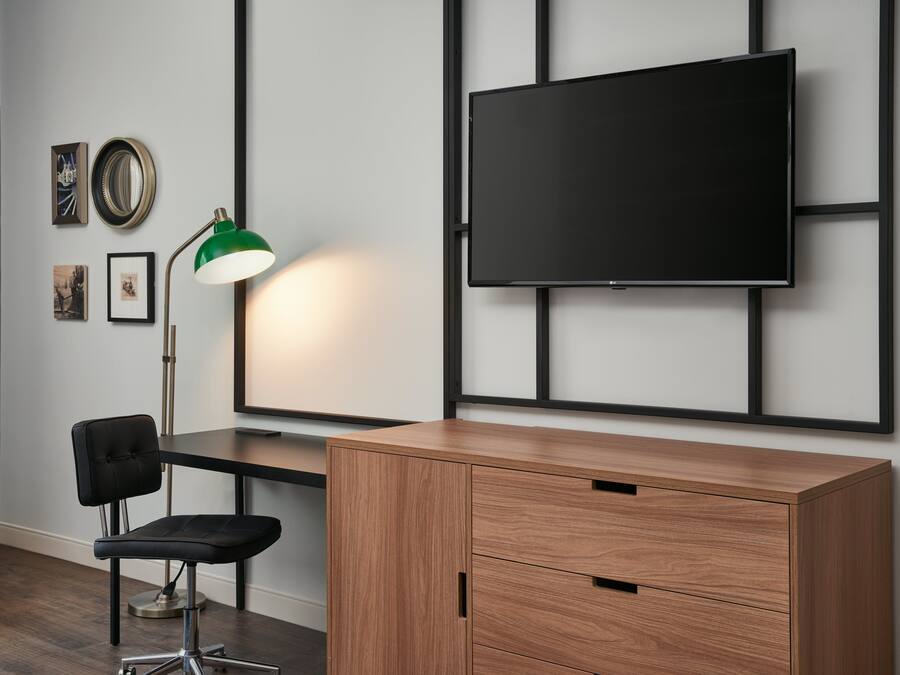A modern room with a wooden desk, a black office chair, a green desk lamp, and a mounted TV on the wall.