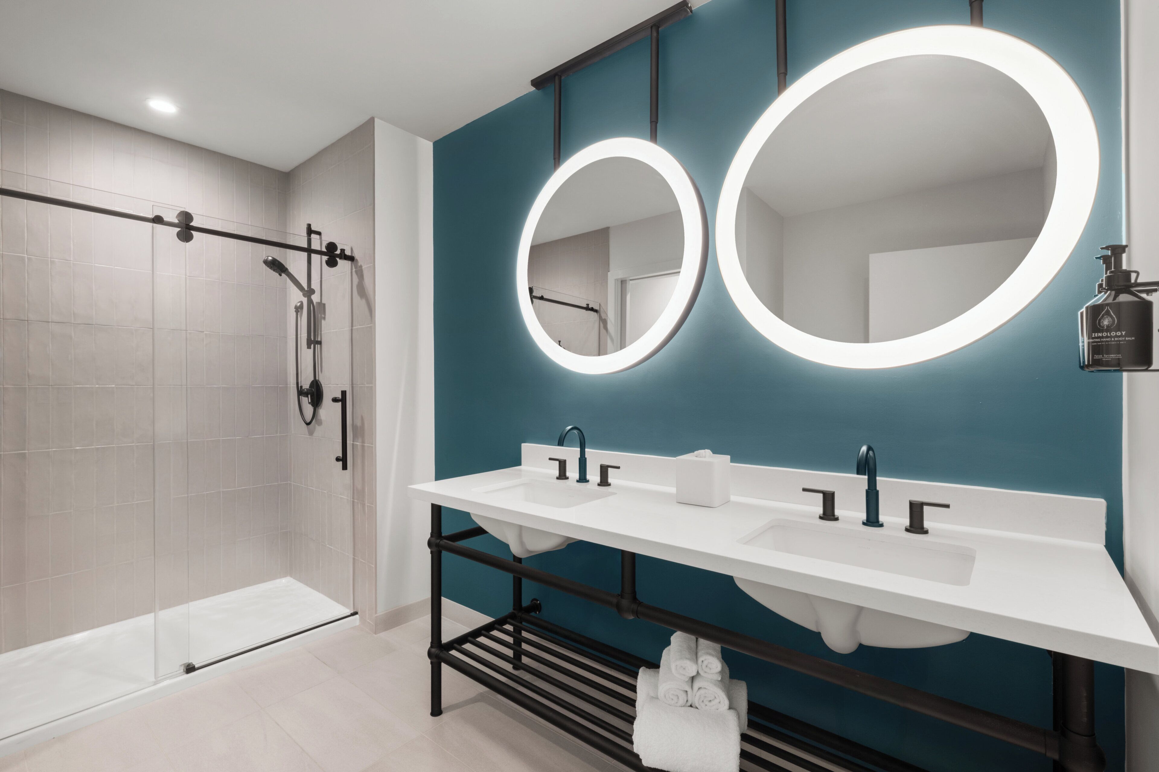 A modern bathroom with a walk-in shower, dual sinks, and a large mirror.