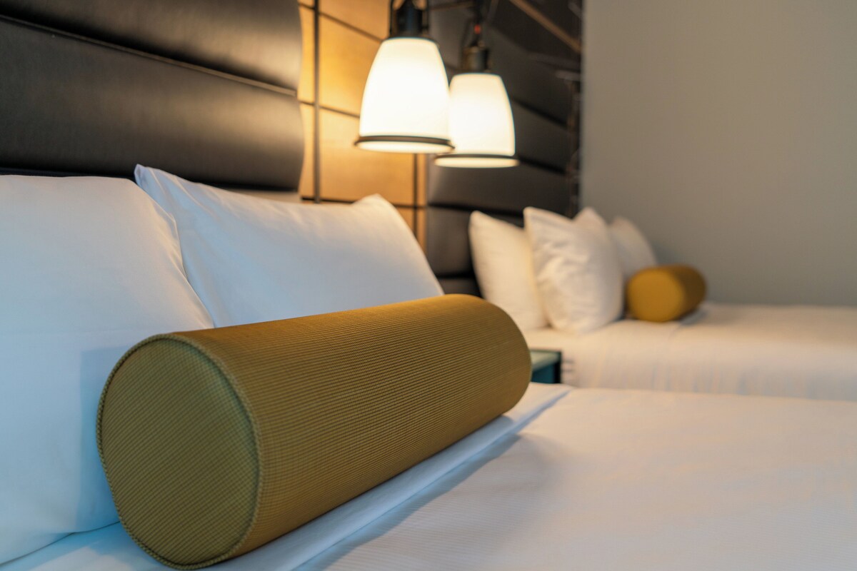 A hotel room with a bed featuring white bedding and a single decorative pillow.