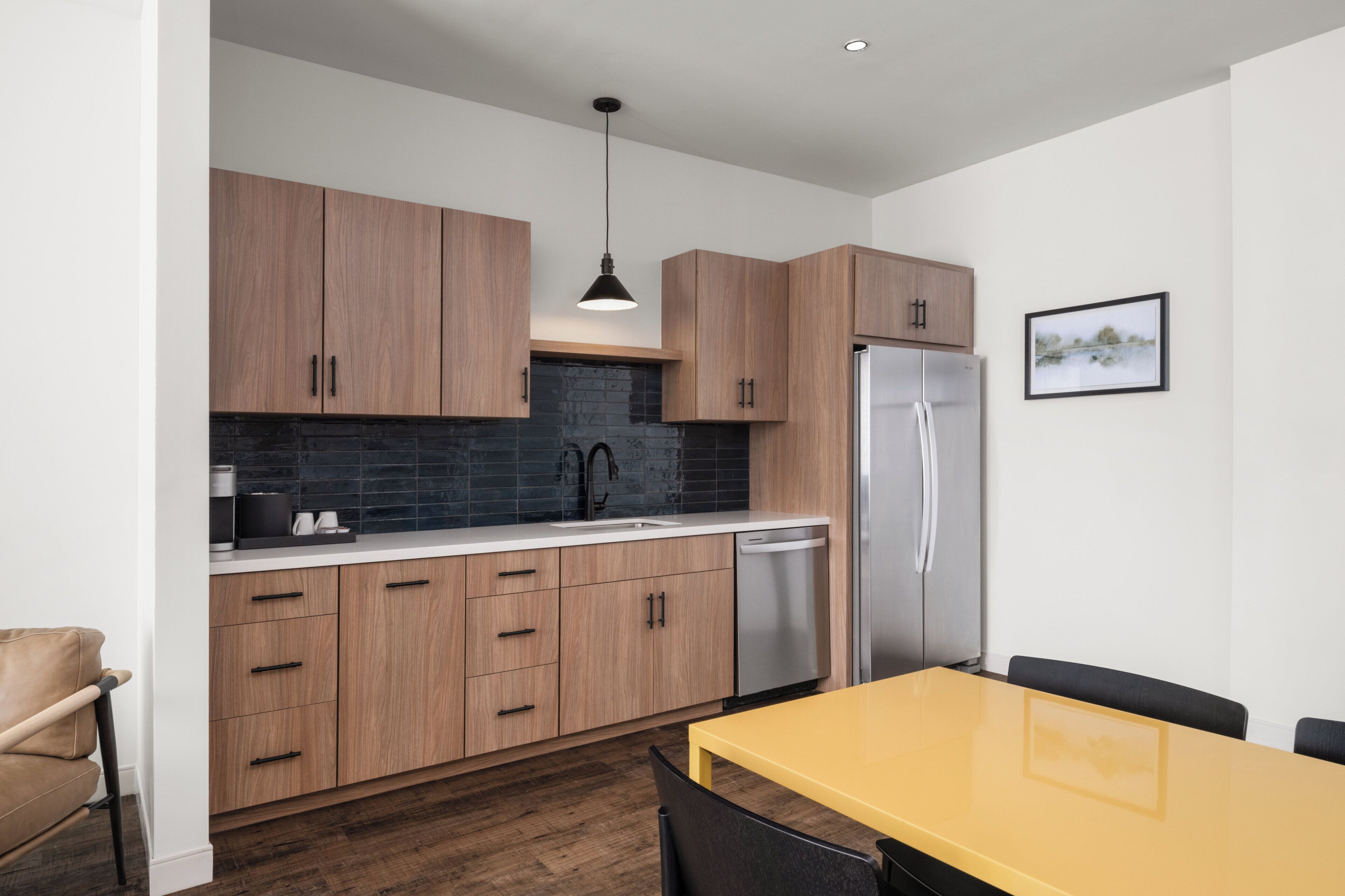 Eine moderne Küche mit Holzschränken, einem Edelstahlkühlschrank und einem gelben Esstisch.