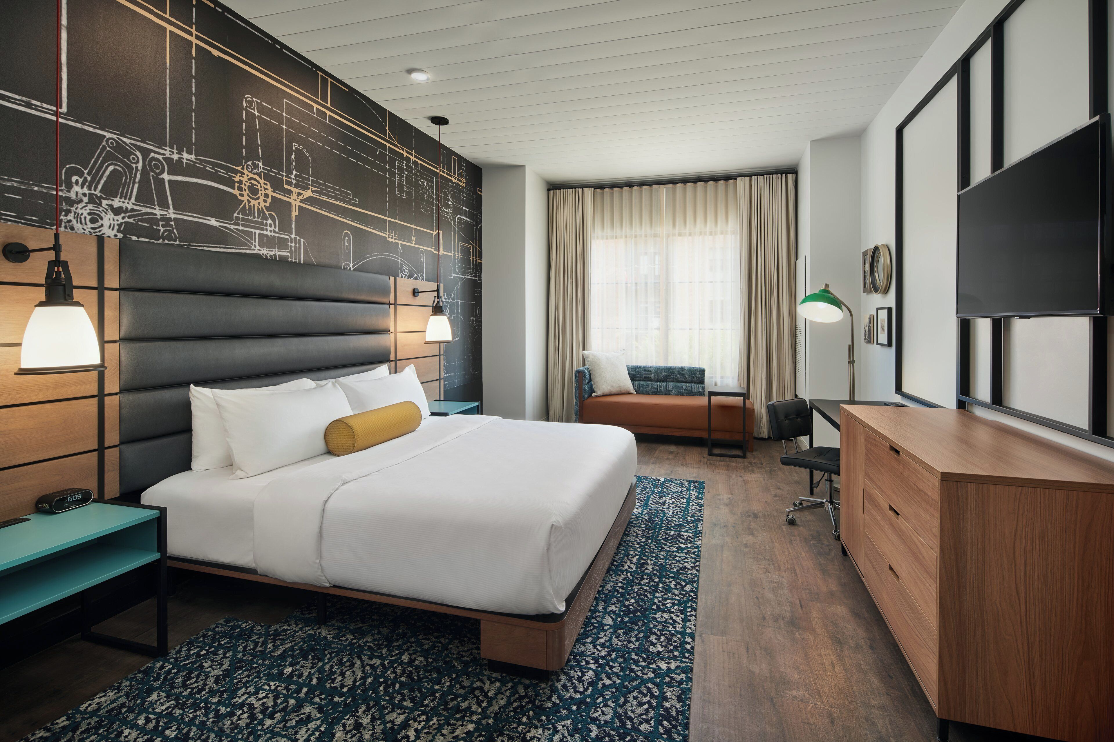 Ein modernes Hotelzimmer mit einem großen Bett, einem Schreibtisch, einem Sessel, einem Fernseher und einem Fenster mit Vorhängen.