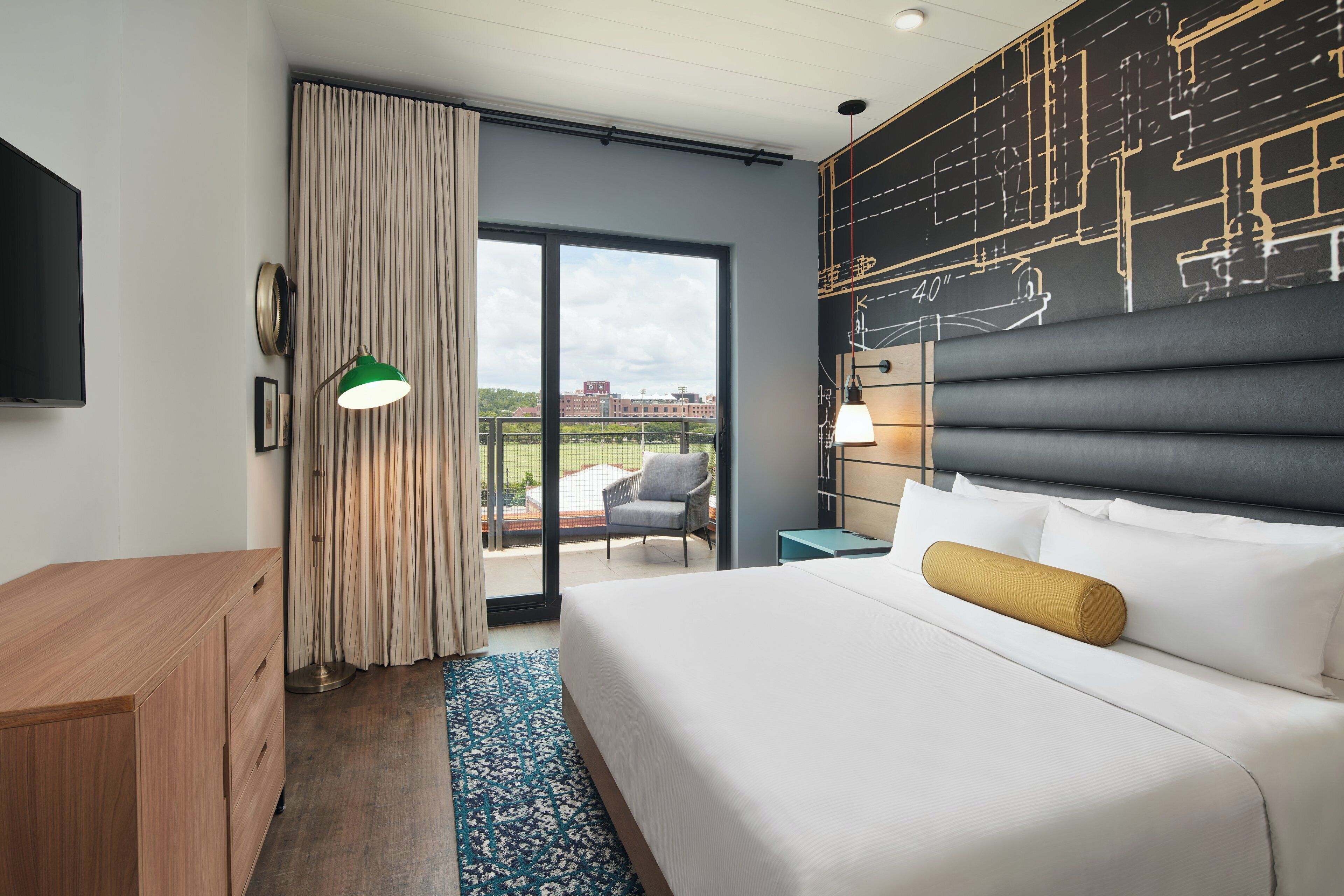 Quarto de hotel com cama grande, escrivaninha, cadeira e varanda com vista para edifícios.