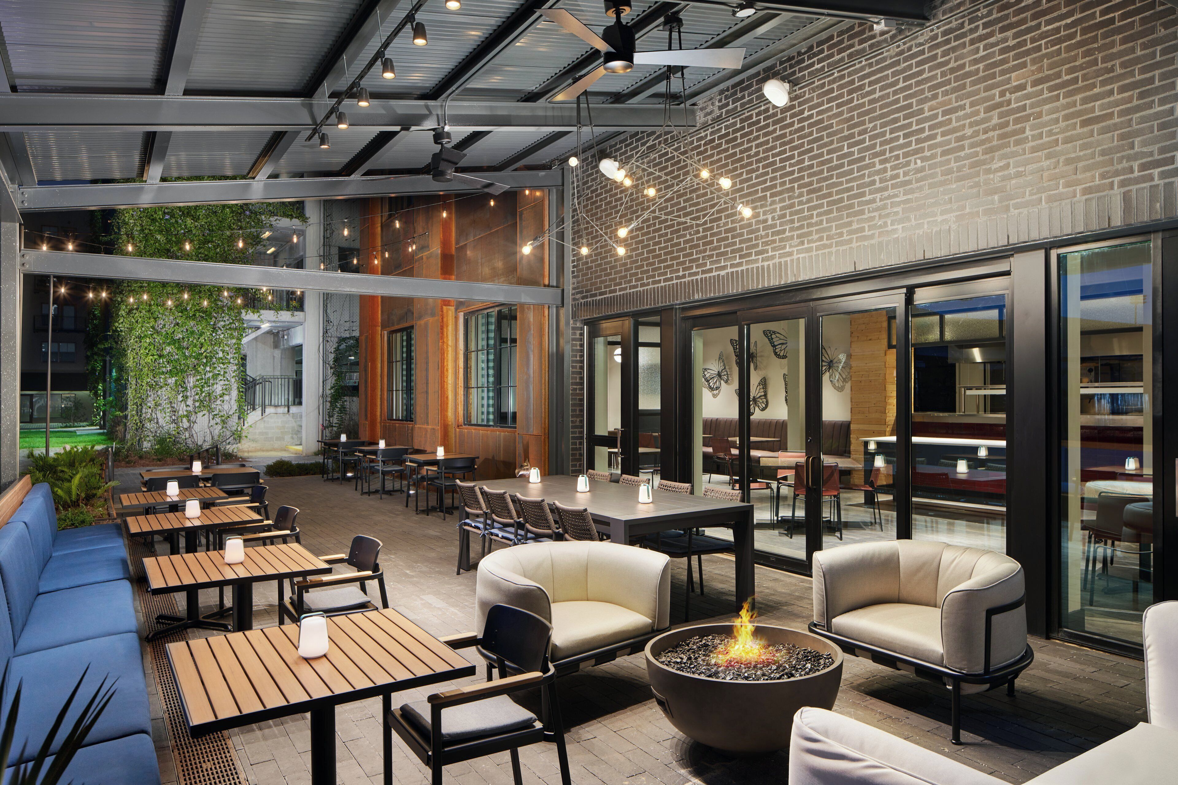 An outdoor seating area with tables and chairs, a fire pit, and a view of the building's interior.