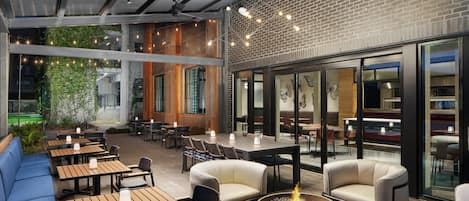Un espacio al aire libre con mesas, sillas, una chimenea y vistas al interior del edificio.