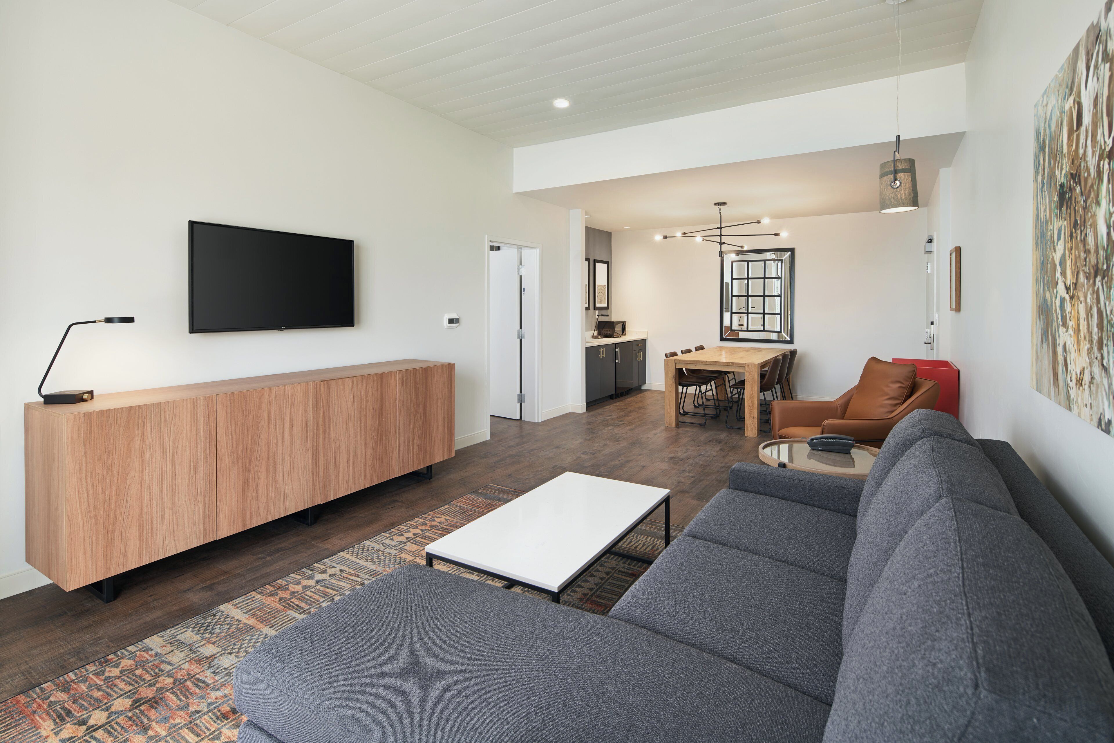 A modern living room with a grey sofa, a wooden coffee table, and a flat-screen TV mounted on the wall.