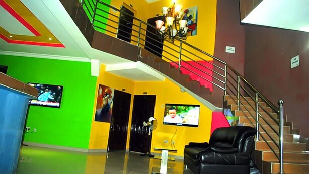 A lobby with a staircase, a black leather sofa, and two televisions on the walls. - Intelligent Hotel and Suites (Port Harcourt)
