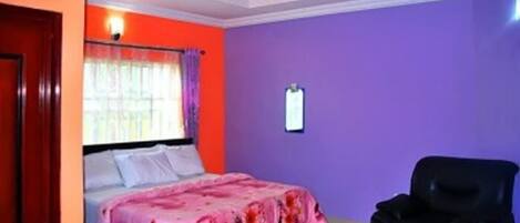 Un dormitorio con cama, una silla y una lámpara fijada a la pared.