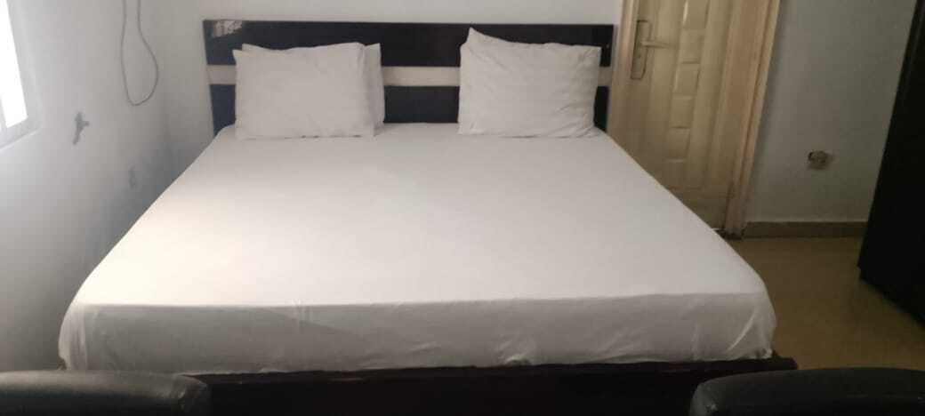 Cama de solteiro com roupa de cama branca em quarto com cabeceira escura e porta branca.