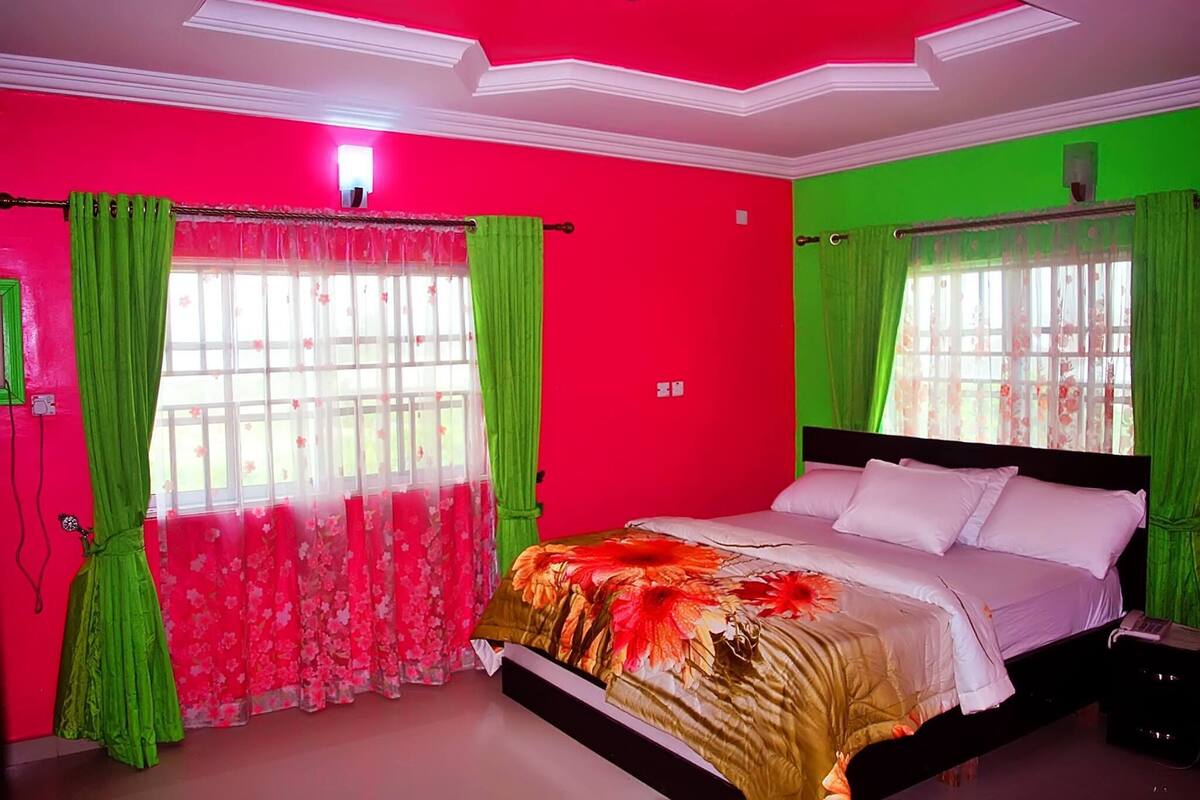 A bedroom with a bed, green curtains, and a window with floral curtains.