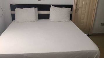 A single bed with a white mattress and two pillows, a dark headboard, and a door to the right.