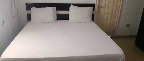 A single bed with a white mattress and two pillows, a dark headboard, and a door to the right.