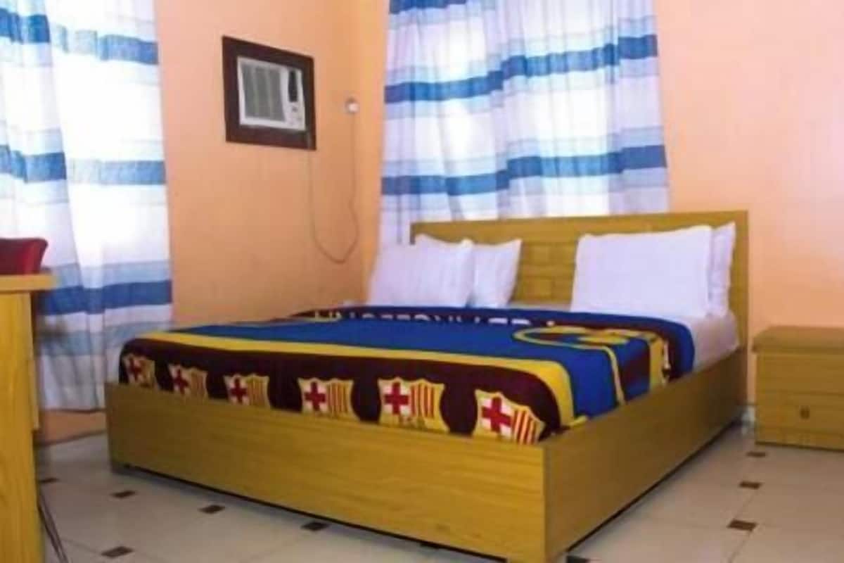 A single bed with a wooden frame and white bedding, a small bedside table, and a wall-mounted light fixture.