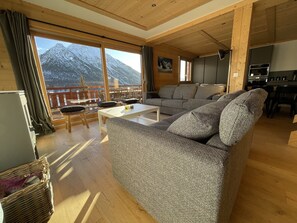 A spacious living room with a large sofa, a coffee table, and a view of snow-capped mountains through large windows.