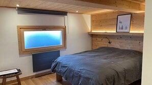 A bedroom with a bed, a window, a wooden headboard, a framed picture, and a small wooden stool. - New charming chalet, 15 to 16 people with panoramic terrace facing south (Montgenèvre)