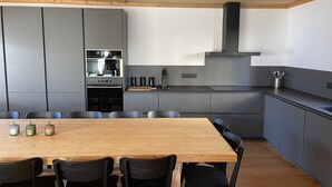 A modern kitchen with grey cabinets, a wooden dining table, and black chairs. - New charming chalet, 15 to 16 people with panoramic terrace facing south (Montgenèvre)