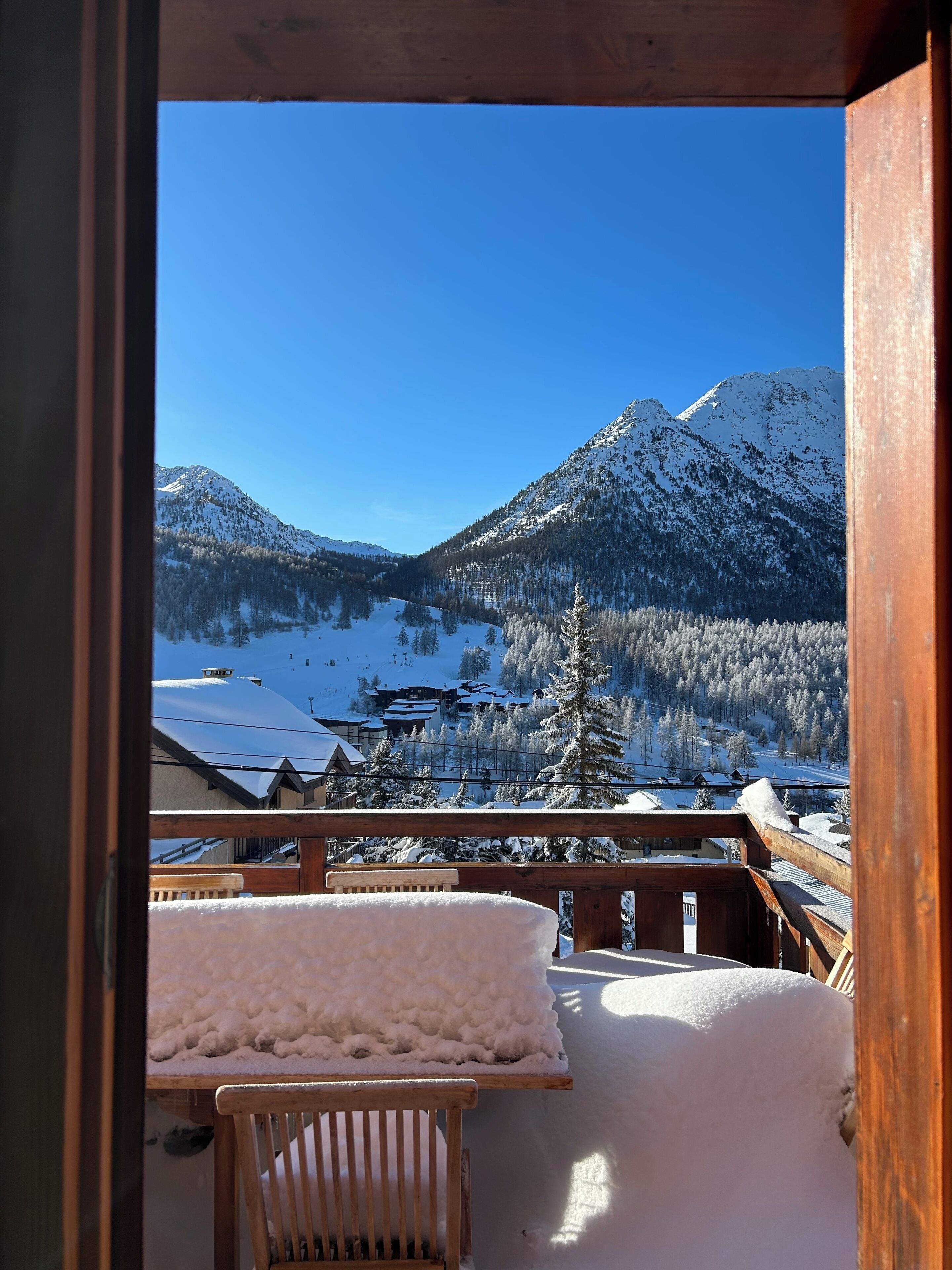 A wooden balcony with a view of a snowy mountain landscape and a ski resort.