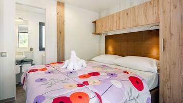 A modern bedroom with a wooden headboard, a floral bedspread, and a white towel sculpture.