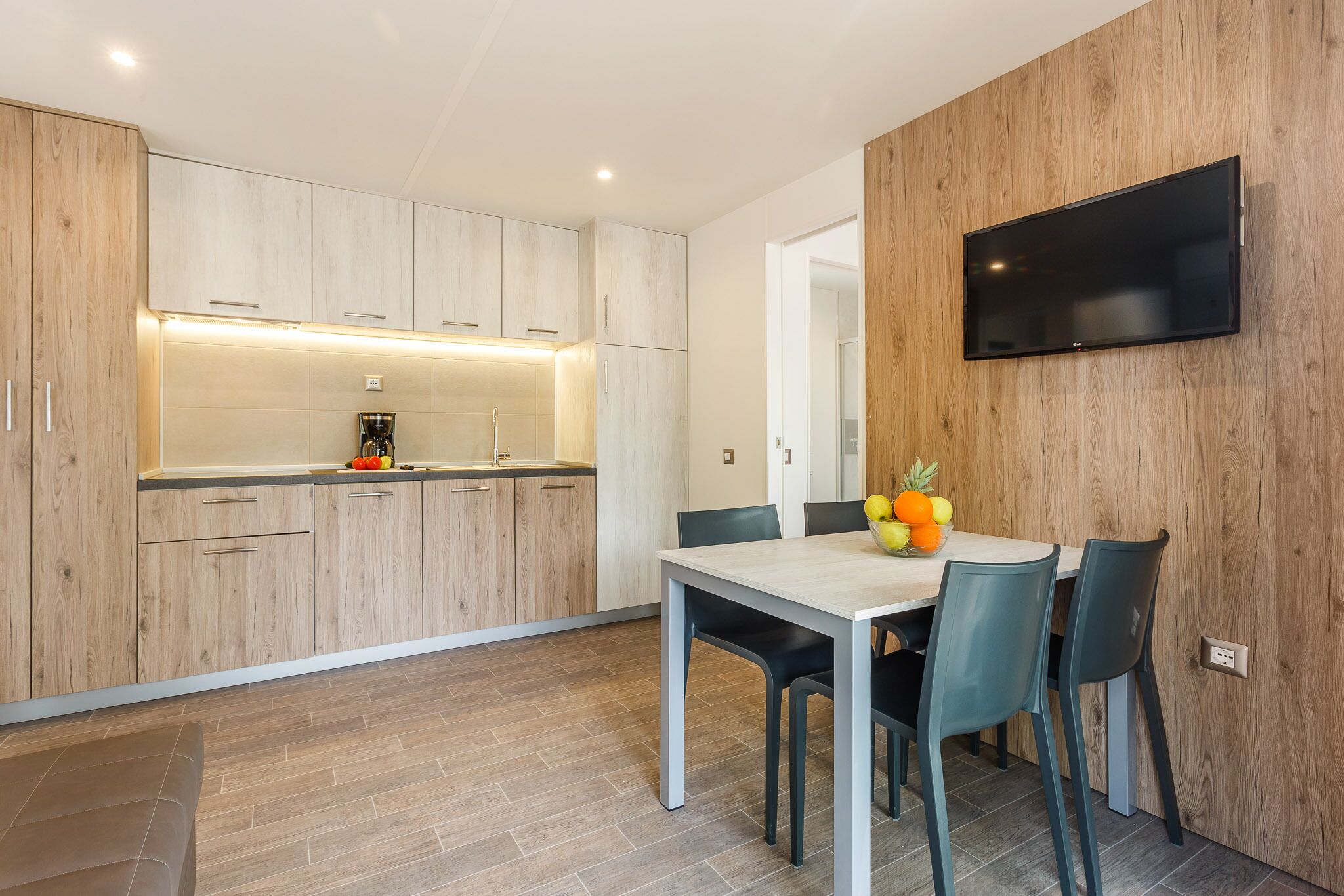 Une cuisine moderne avec des meubles en bois, un four encastré et un coin repas comprenant une table et des chaises.