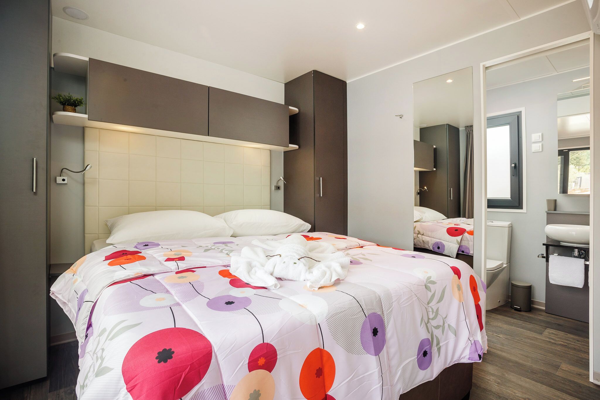 Ein modernes Schlafzimmer mit einem großen Bett, einem Nachttisch, einem Kleiderschrank und einem durch eine offene Tür erreichbaren Badezimmer.