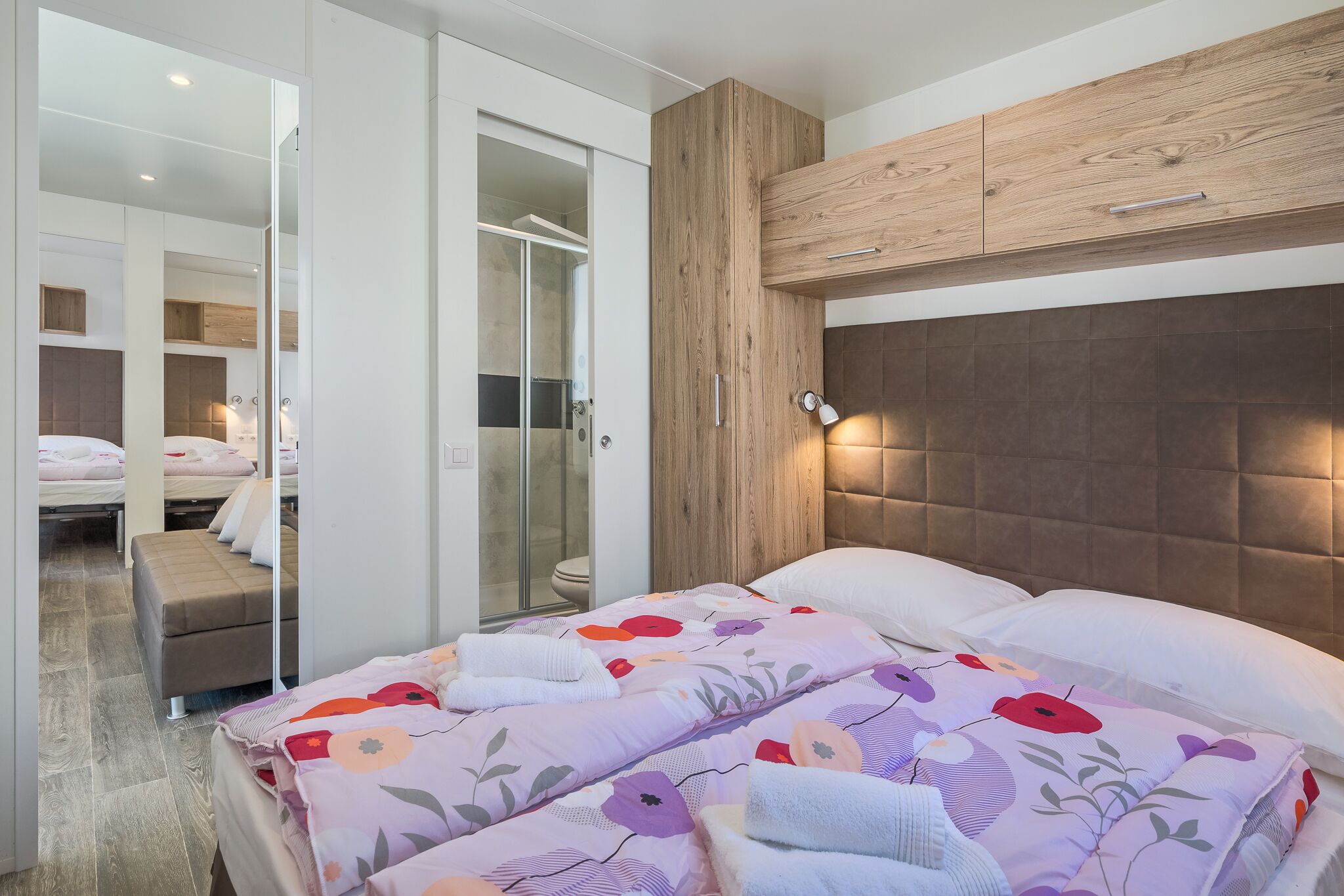 Een moderne hotelkamer met een groot bed, een houten hoofdbord en een douchecabine van glas.