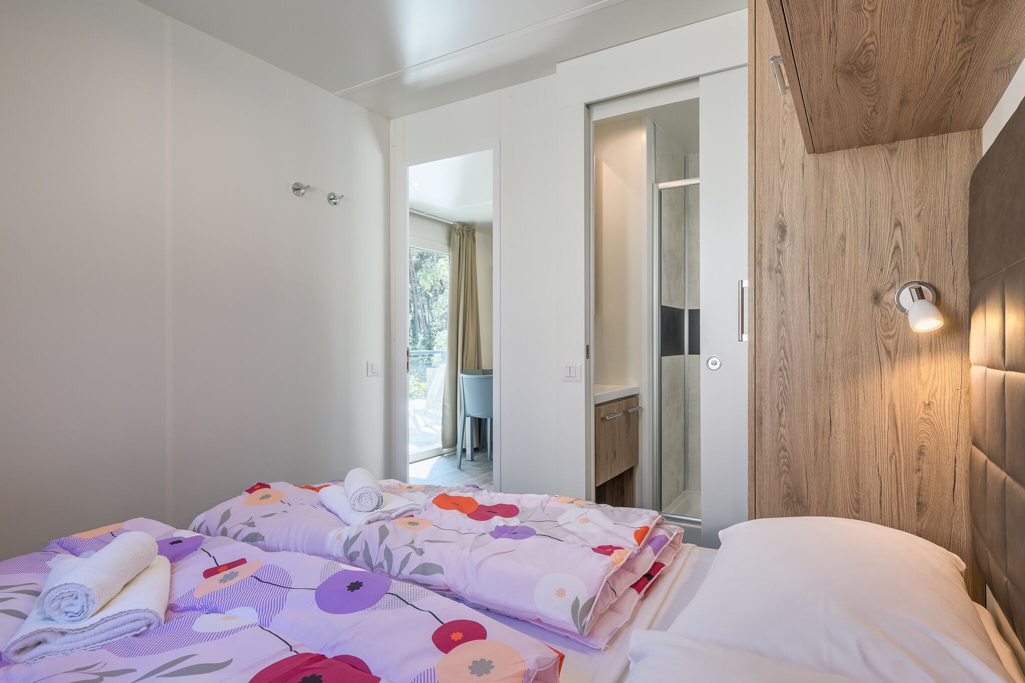 A bedroom with two beds, a wooden headboard, and a bathroom visible through an open door.