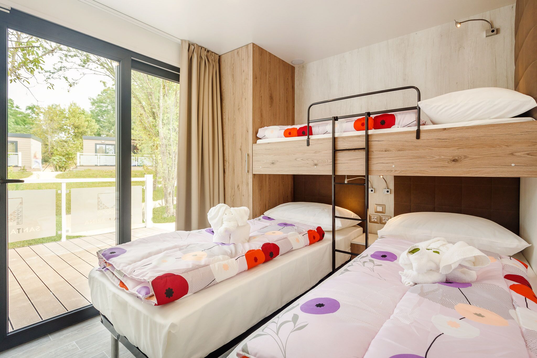 Ein Schlafraum mit Etagenbetten, einem großen Fenster, einer Holzwand und einem Bett mit Blumenmuster-Bettwäsche.