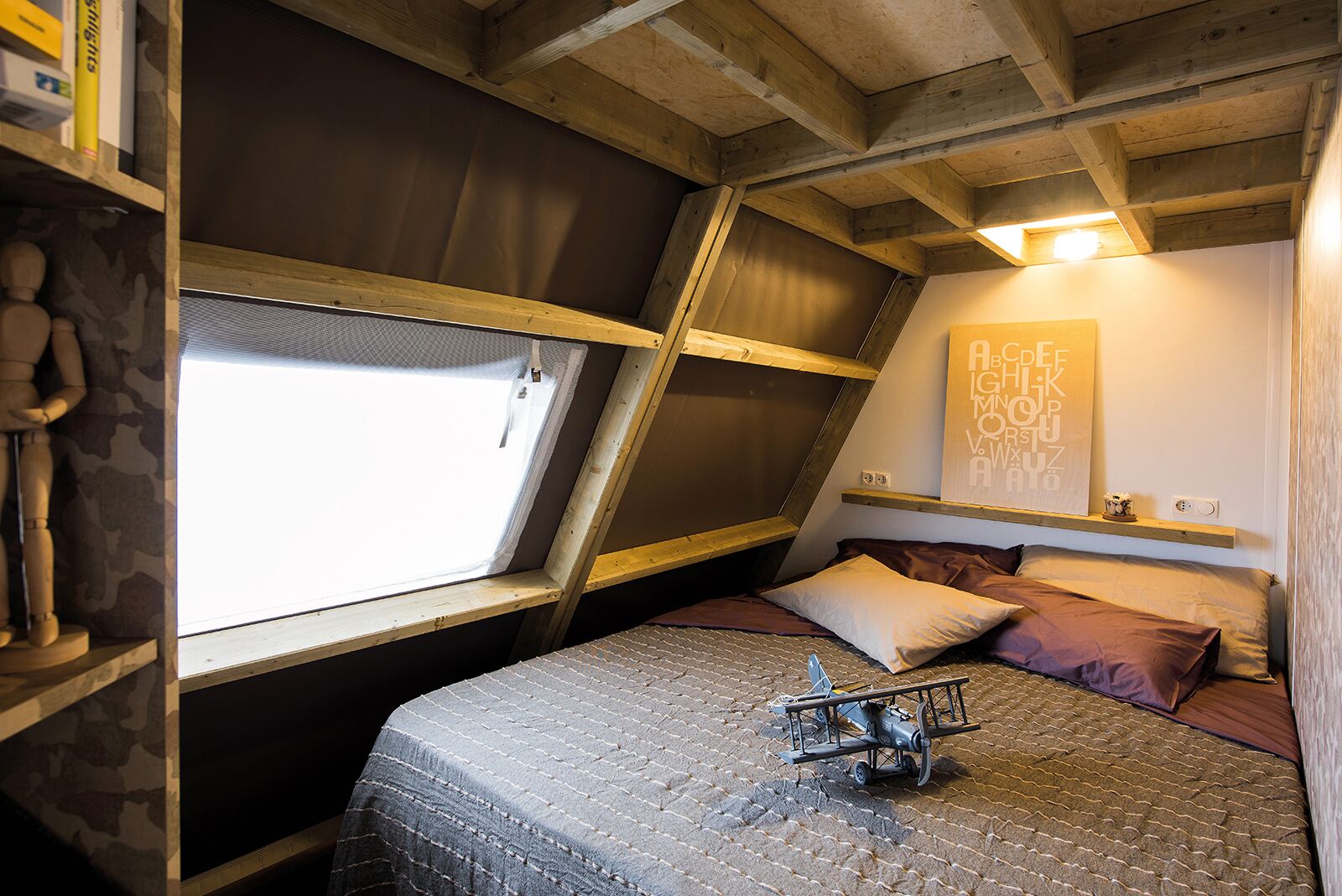 A bedroom with a sloped ceiling, a bed with patterned bedding, a small airplane model, and a wall with a geometric design.