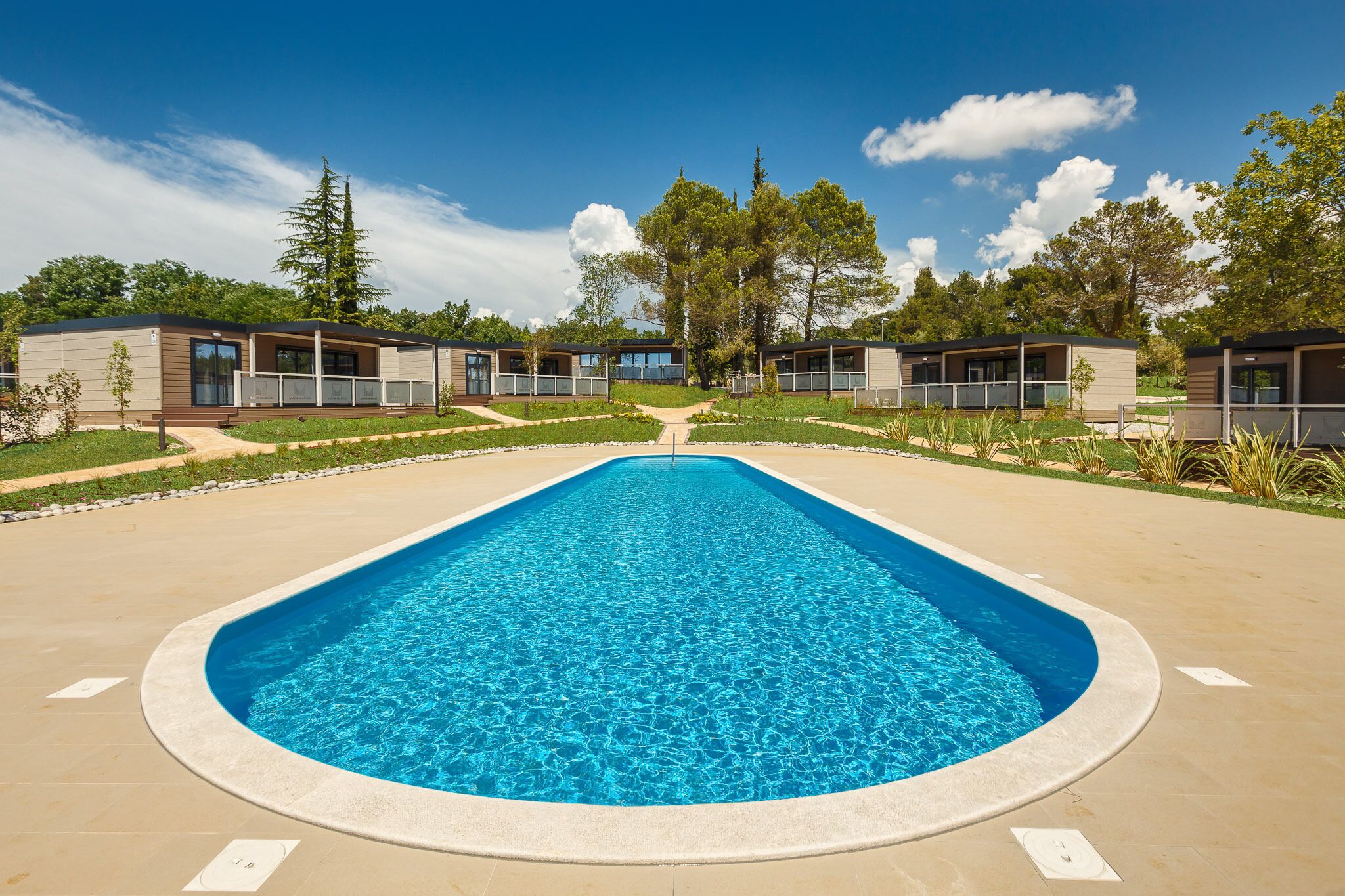 A rectangular swimming pool with a clear blue center, surrounded by a paved walkway.