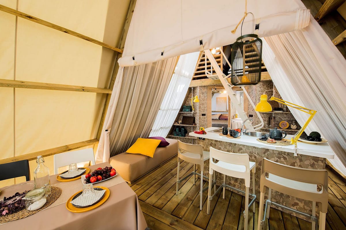 Una tienda acogedora y bien iluminada con comedor, kitchenette y zona de estar confortable con cojines.