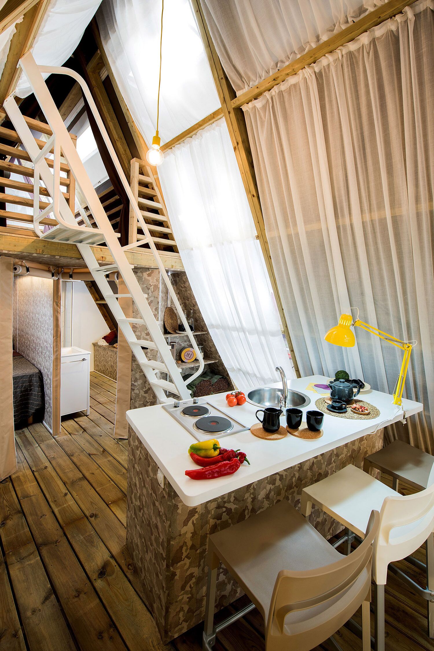 Une pièce mansardée chaleureuse avec un escalier en bois, une petite kitchenette et un coin repas comprenant une table et des chaises.