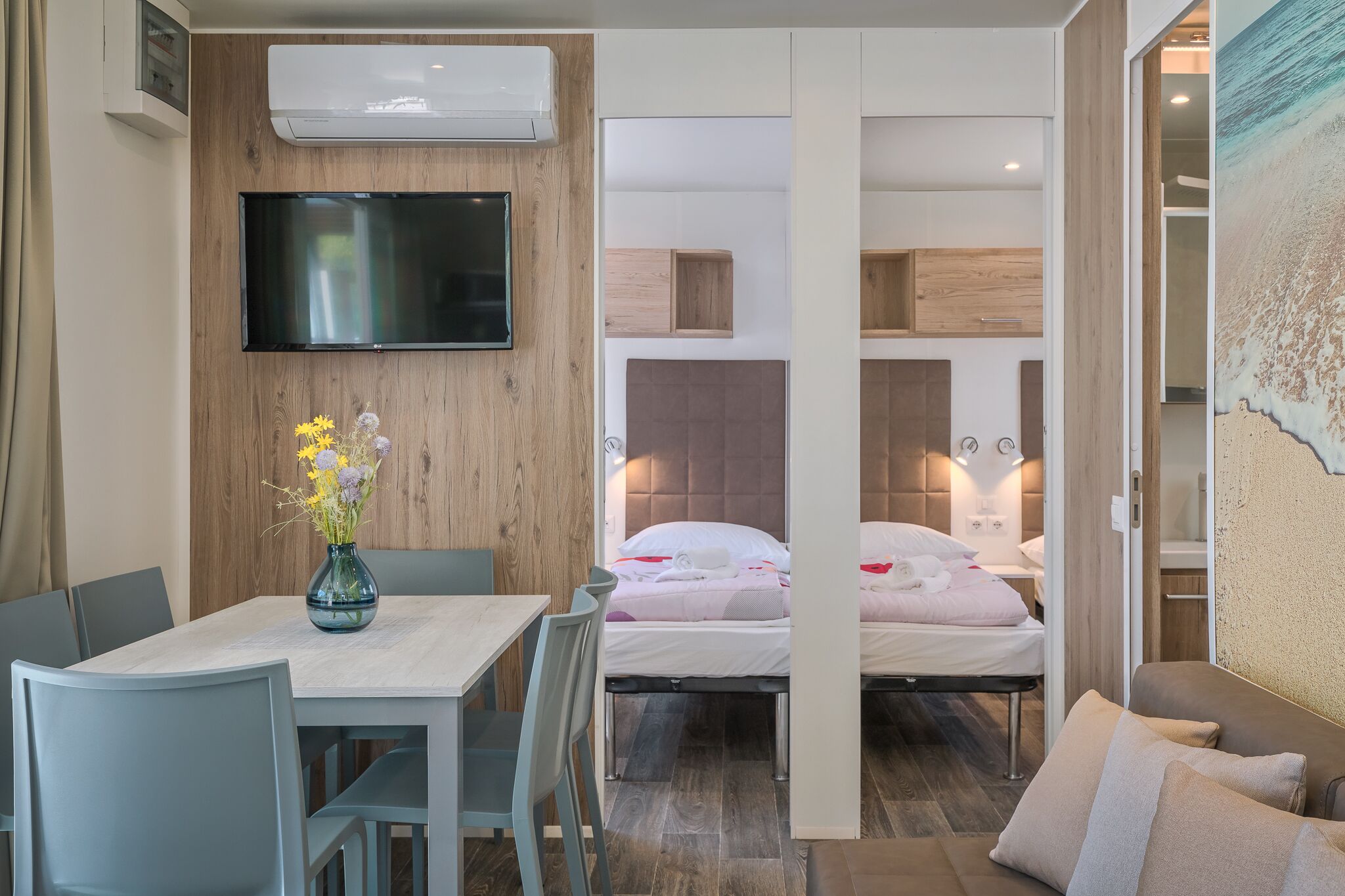 Una habitación compacta con una mesa de comedor, un televisor montado en la pared, una cama con cabecera y un pequeño rincón de descanso.