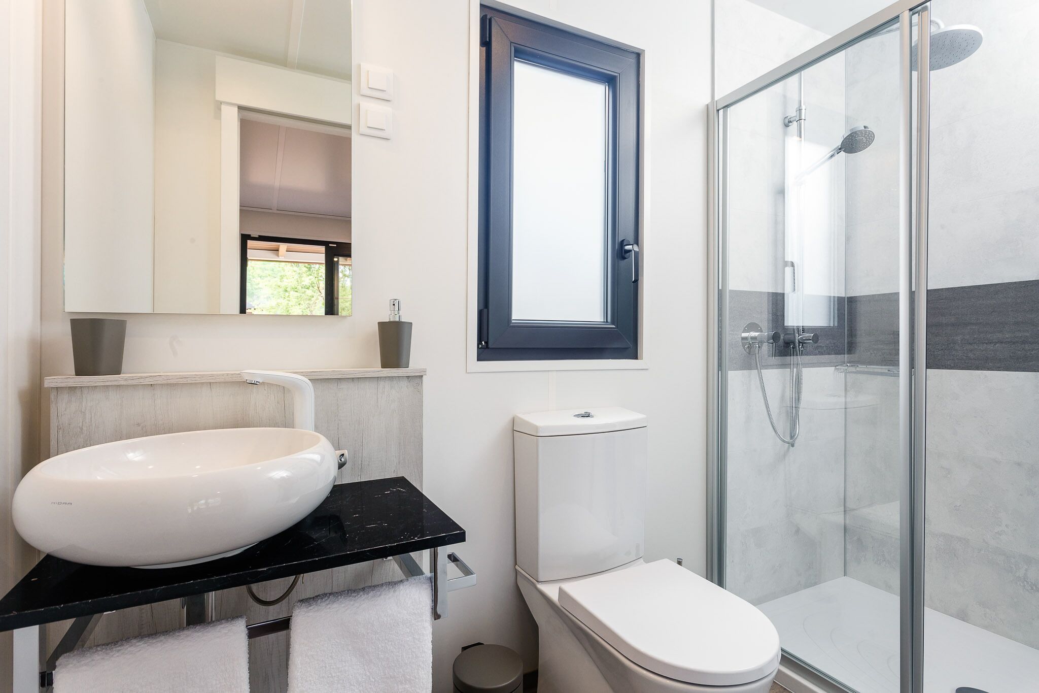 A modern bathroom with a white sink, black countertop, white toilet, and a glass-enclosed shower.