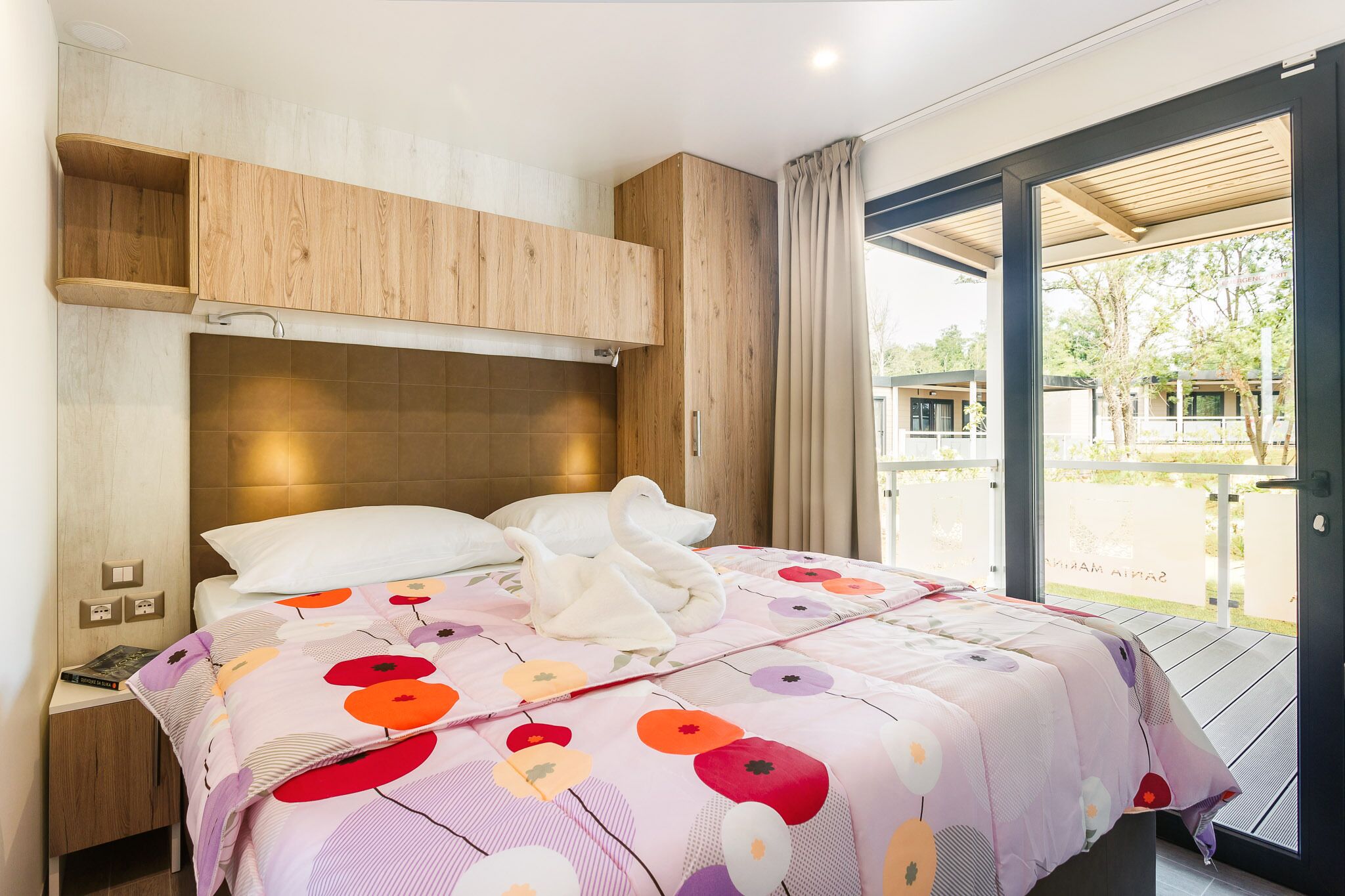 A bedroom with a bed, wooden headboard, and a view of a garden through a glass door.