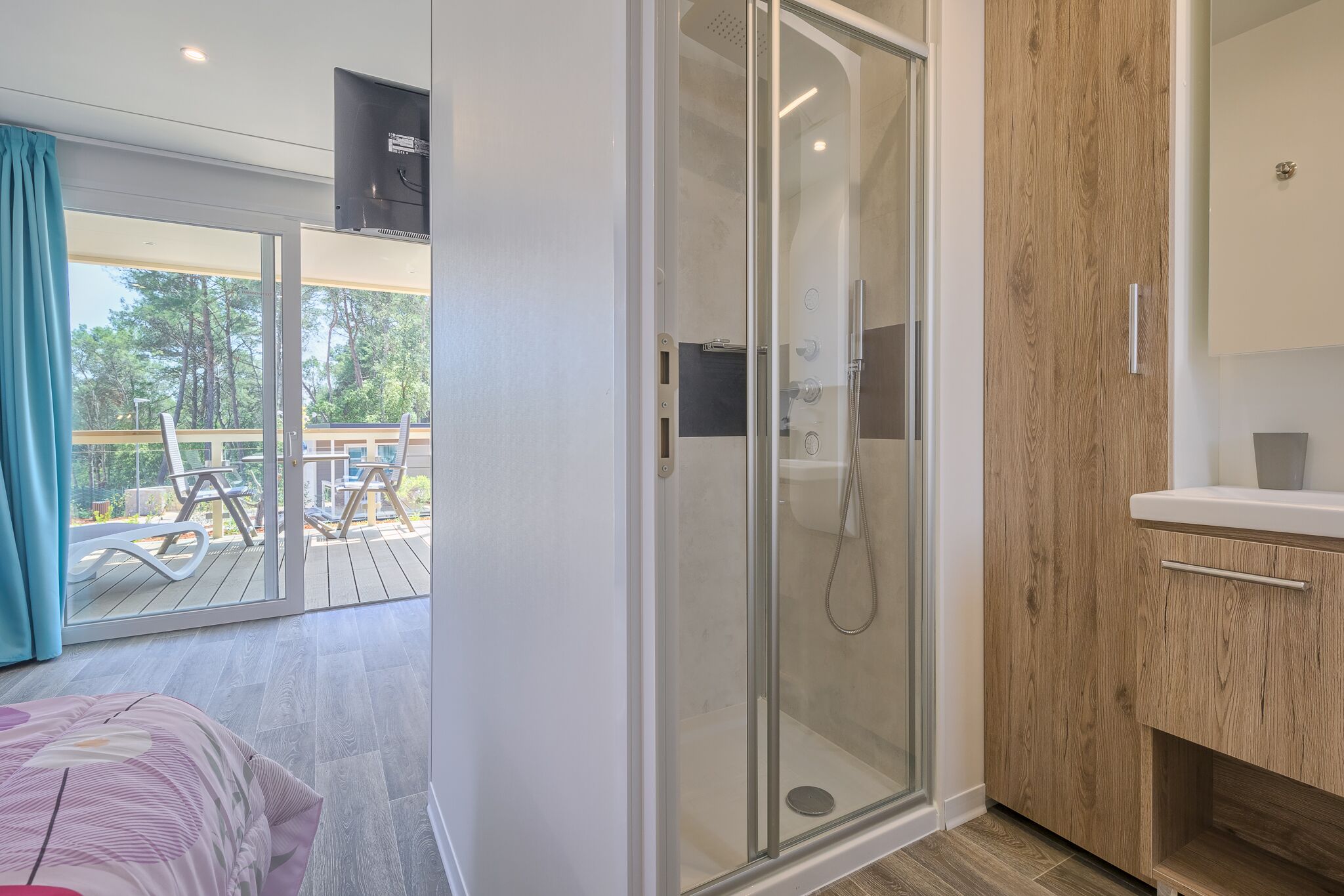 Un baño moderno con cabina de ducha de vidrio, muebles de madera y un balcón con mobiliario exterior.