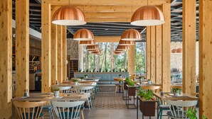 Un restaurante con vigas de madera, varias mesas, sillas y lámparas colgantes de cobre.