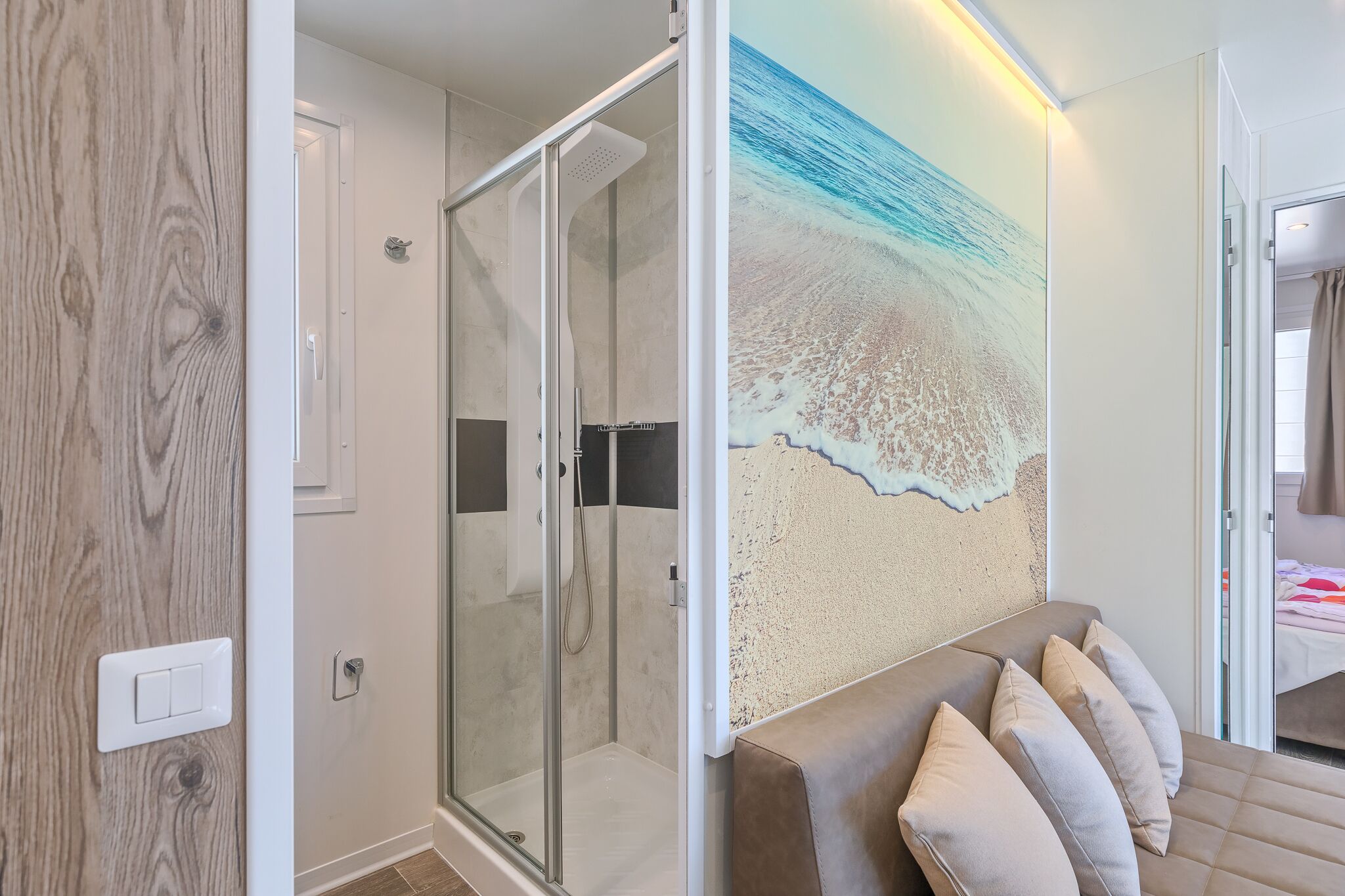 A modern bathroom with a glass shower enclosure, a wall-mounted towel rack, and a large beach-themed mural.