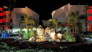 A nighttime outdoor area with stone planters, palm trees, and a blue bench.