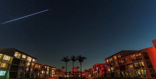 Vista noturna de um hotel com vários edifícios, céu estrelado e uma estrela cadente visível.