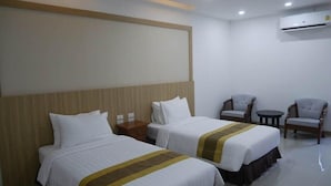 Ein Hotelzimmer mit zwei Betten, einem hölzernen Kopfteil, einem kleinen Tisch, zwei Stühlen und einer Klimaanlage.