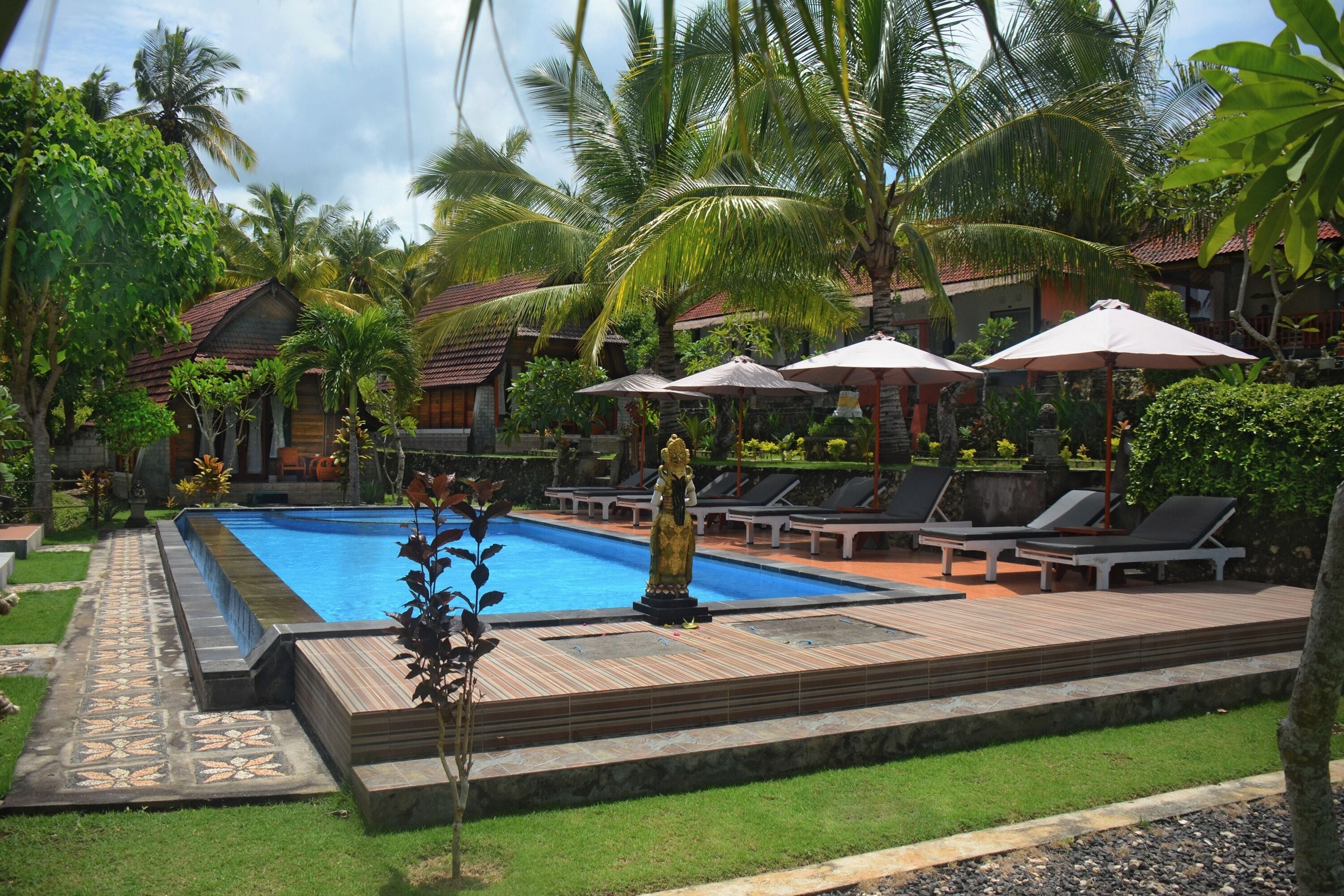A pool area with lounge chairs and umbrellas, surrounded by palm trees and a wooden deck.