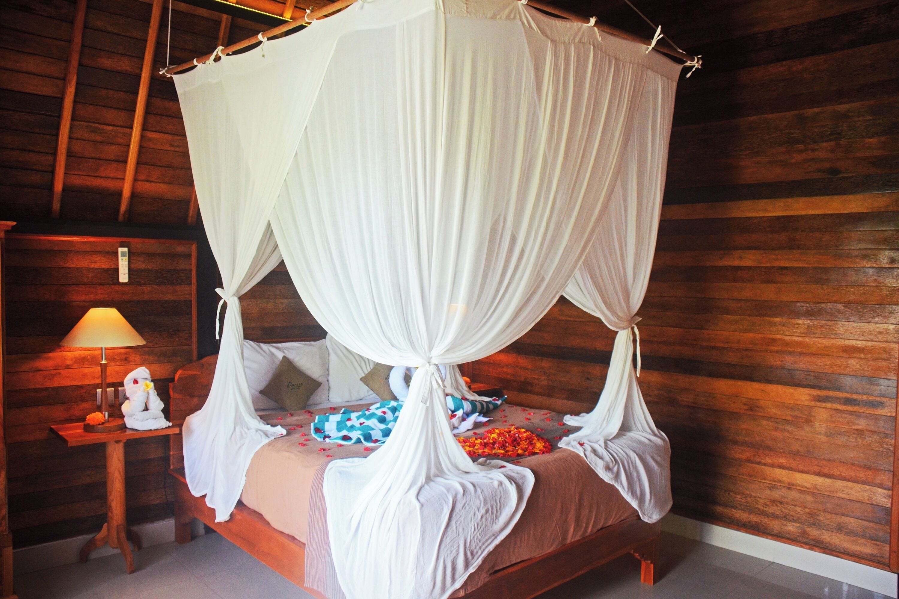 A four-poster canopy bed with a wooden headboard, a bedside table with a lamp, and a small decorative item.