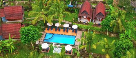 Vista aérea de un complejo turístico con piscina, palmeras y arquitectura tradicional.