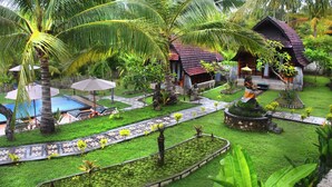 A tropical resort with a swimming pool, palm trees, and a small house with a red roof. - Mamaras Guest House (Penida Island)
