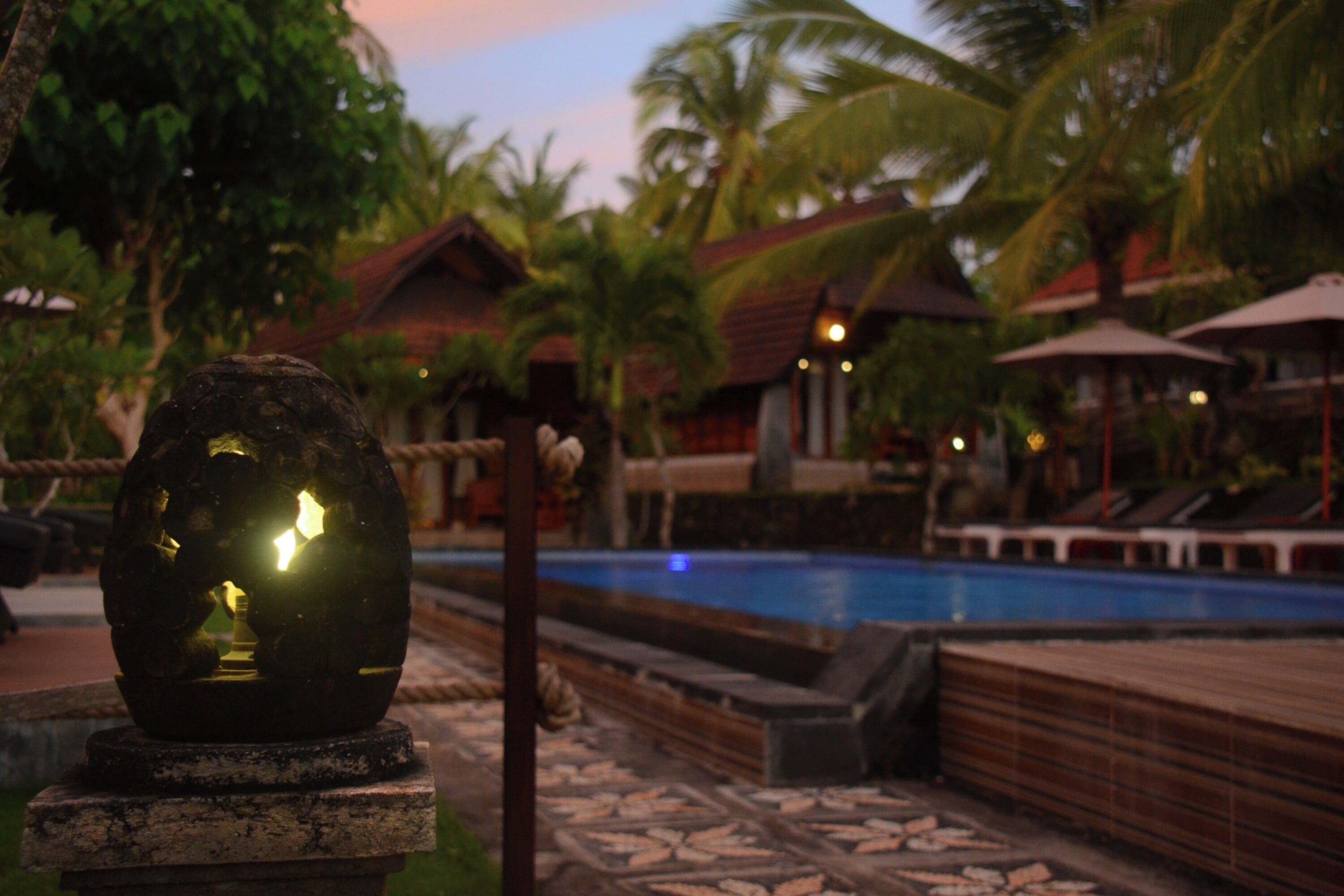 A pool area with a decorative stone structure, palm trees, and a building with a red roof.