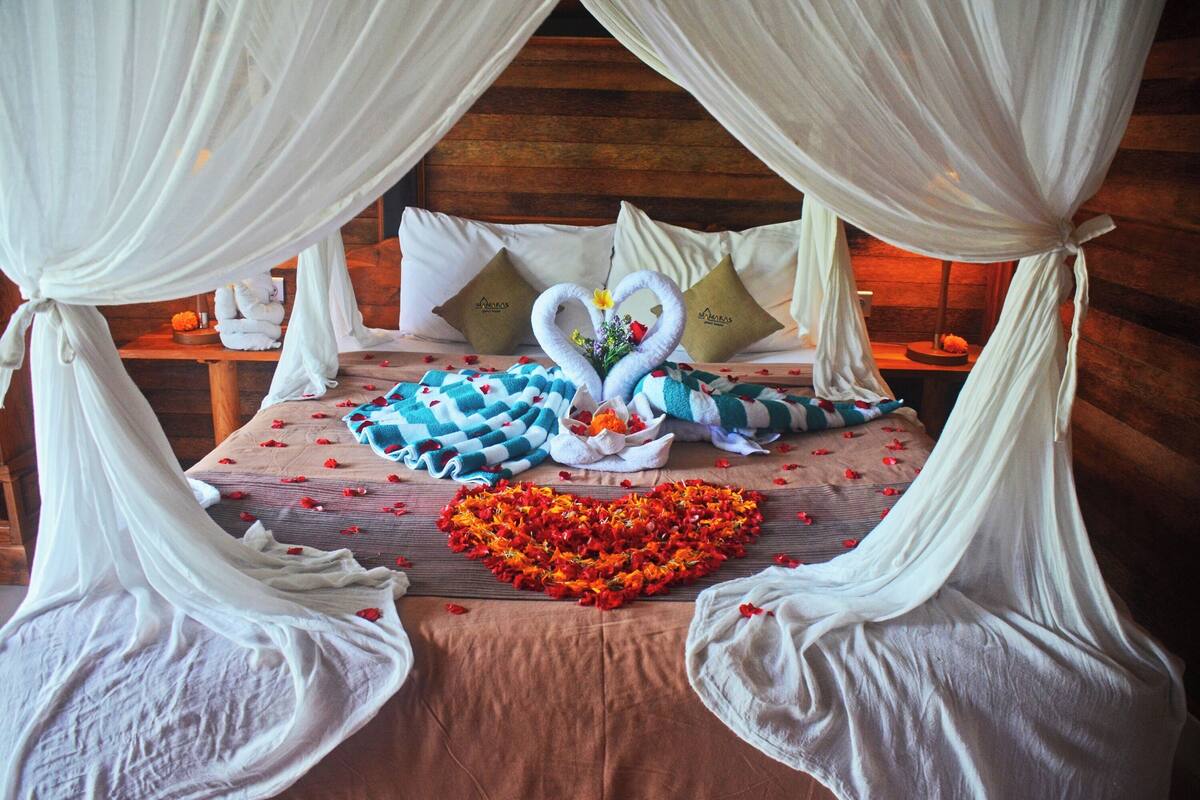 A bed with a heart-shaped flower arrangement, two swan-shaped pillows, and a wooden headboard.