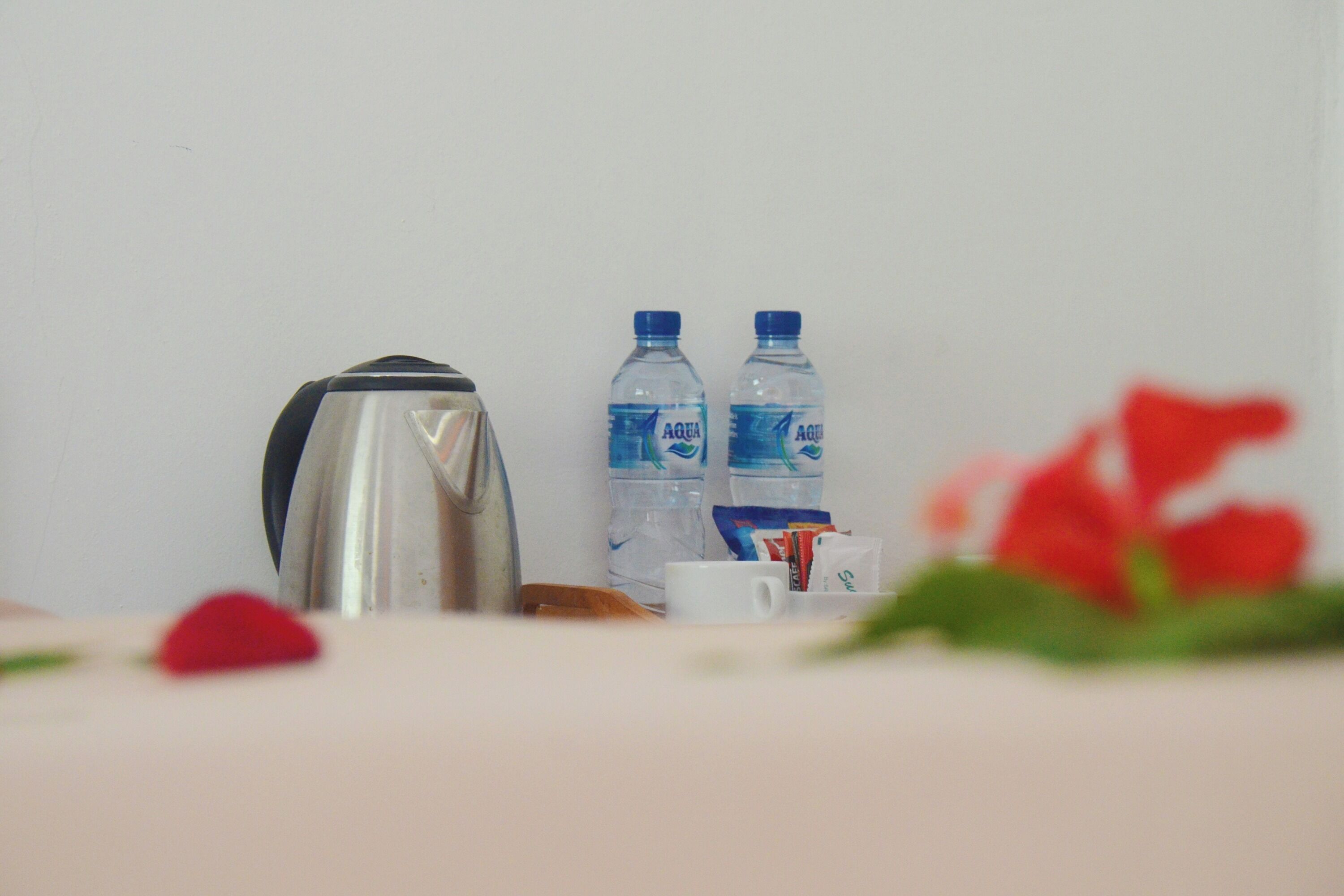 Una cocina americana con hervidor, dos botellas de agua, una taza de café y un sobre de azúcar sobre una encimera.