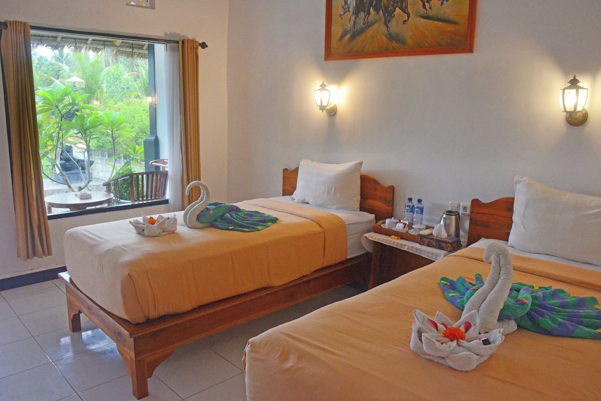 A hotel room with two beds, a window with curtains, a painting on the wall, and a table with toiletries.