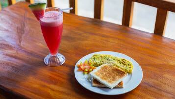 A wooden table with a plate of food and a glass of red drink.