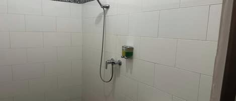 Un baño pequeño y con azulejos, con ducha, inodoro y dispensador de jabón.