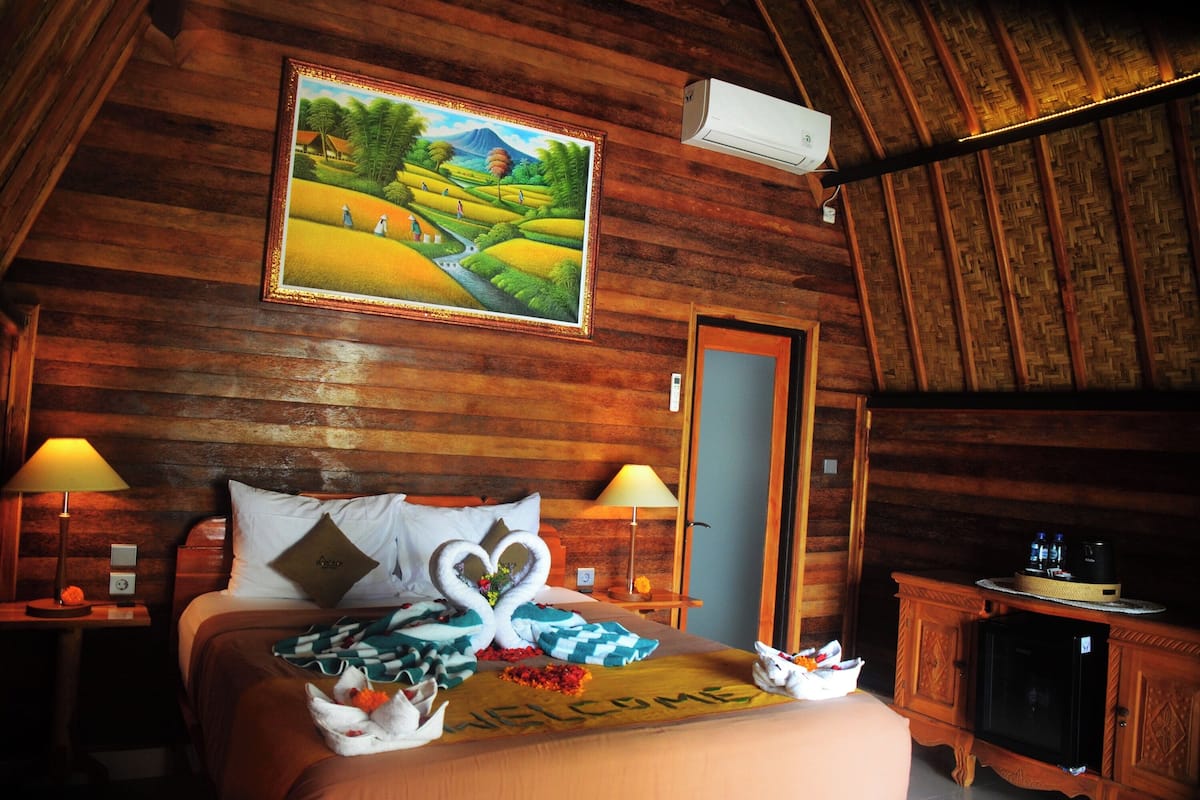 A wooden cabin-style room with a bed, two bedside lamps, a painting, a TV, and a wooden cabinet.